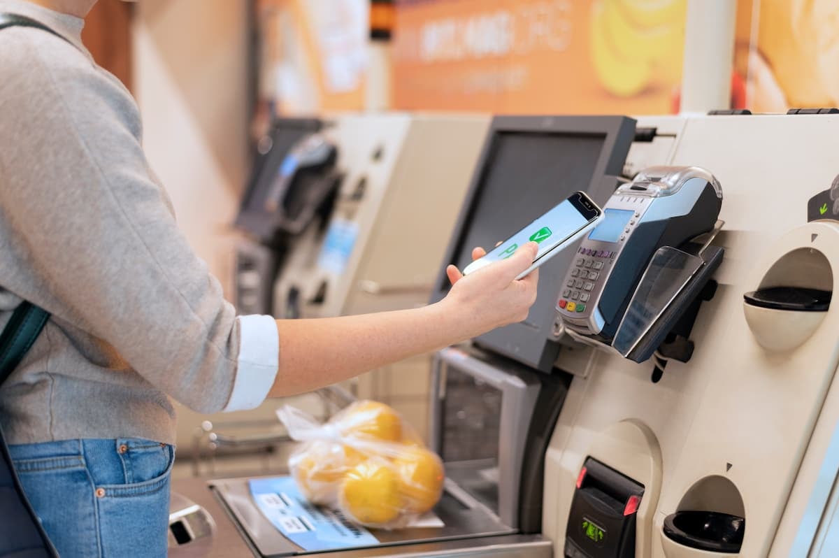 Pessoa realizando um pagamento por aproximação com smartphone em um terminal de checkout, demonstrando o uso da tecnologia NFC para transações rápidas e sem contato.