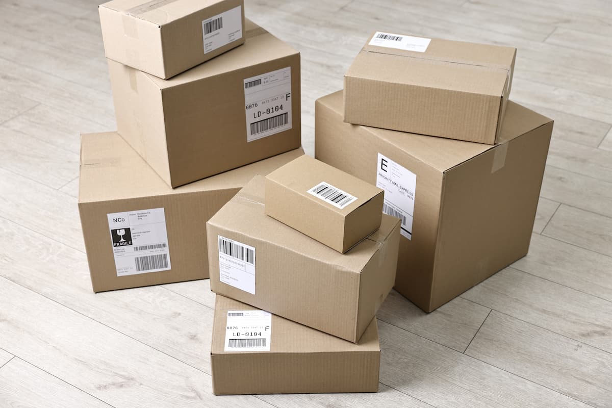 Pilhas de caixas de papelão de diferentes tamanhos organizadas sobre piso claro, todas com etiquetas logísticas e códigos de barras visíveis na parte externa das embalagens.
