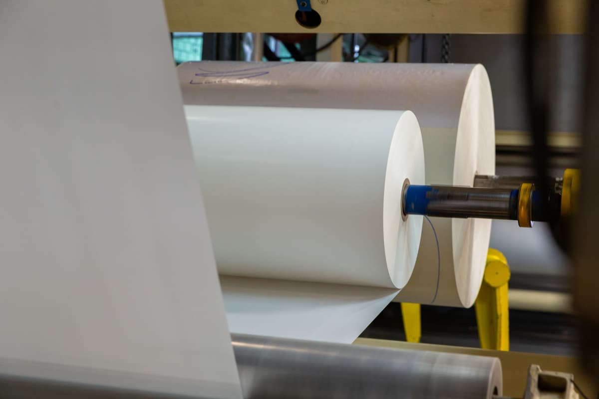 Rolls of white release liner for PSA labels being processed on an industrial production machine.