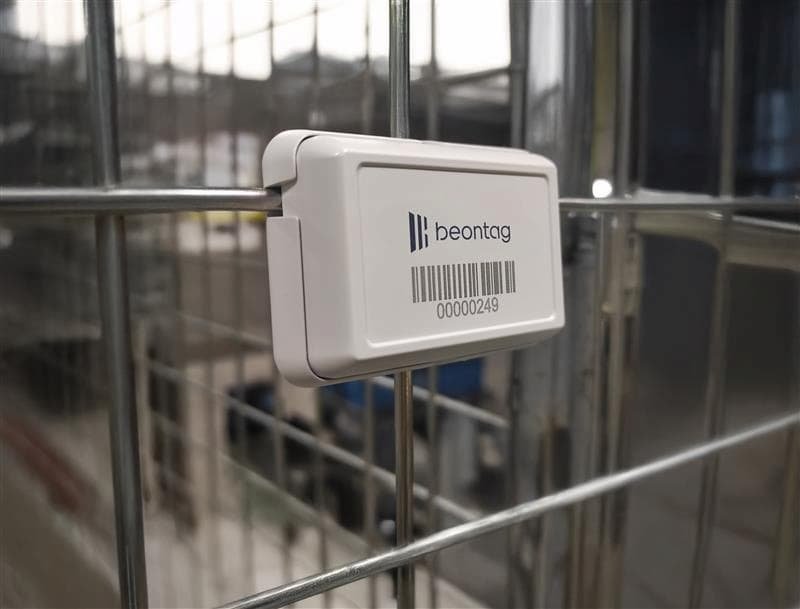 Etiqueta BLE (Bluetooth Low Energy) branca da Beontag fixada em uma estrutura metálica tipo grade, com código de barras e numeração visível, utilizada para rastreamento e identificação em ambiente industrial.